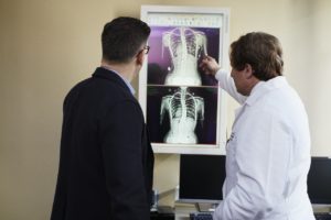 doctor-pointing-x-ray-result-beside-man-wearing-black-suit-2182972